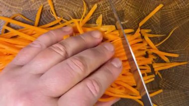 Şef, tahta kesme tahtasının üzerinde bıçakla doğranmış havuç doğruyor..