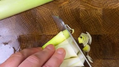 Şef pırasa sapını tahta kesme tahtasında satırla keser..