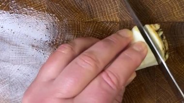 Bir aşçı, ağaç kesme tahtasına saplanmış bir bıçakla maydanoz kökü doğruyor..