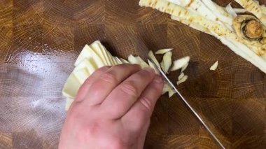 Bir aşçı, ağaç kesme tahtasına saplanmış bir bıçakla maydanoz kökü doğruyor..