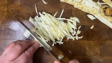 Bir aşçı, ağaç kesme tahtasına saplanmış bir bıçakla maydanoz kökü doğruyor..