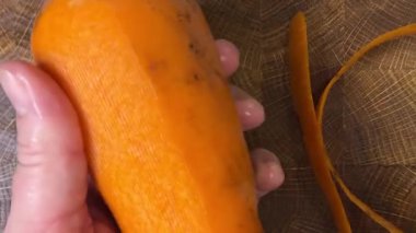 Ahşap kesme tahtasına havuç soyan bir kadın..