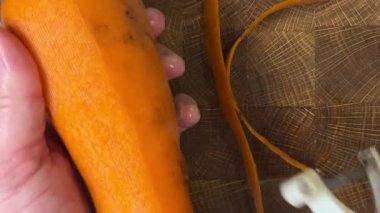 Ahşap kesme tahtasına havuç soyan bir kadın..