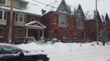 TORONTO, Kanada - 16 Şubat 2025: Toronto, Ontario, Kanada 'da karlı kış. İki katlı tuğlalı özel evler, ıssız bir cadde ve kar yağarken yavaşça geçen bir araba..
