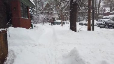 Toronto, Ontario, Kanada 'da karlı bir kış. İki katlı binaların olduğu bir yerleşim bölgesinde insanlar dar bir patika boyunca birbirlerine doğru yürüyorlar..