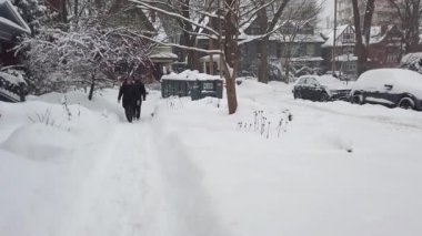TORONTO, Kanada - 16 Şubat 2025: Toronto, Ontario, Kanada 'da karlı kış. İnsanlar, eski iki katlı binaların bulunduğu bir yerleşim bölgesinde kar fırtınası sırasında kar yığınları arasında dar bir yolda birbirlerini geçmeye çalışıyorlar..