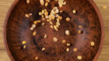 Kurutulmuş bezelyeler, tahtadan bir meşe ağacına karşı kahverengi bir seramik kaseye dökülür. Üst Manzara. Yavaş çekim.
