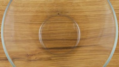 Kabuk şeklindeki makarna, cam şeffaf bir kaseye, tahta bir meşe tahtasına dökülür. Üst Manzara. Yavaş çekim.