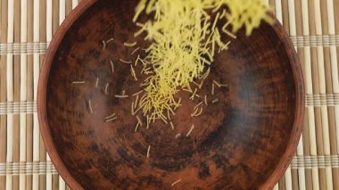 İnce küçük makarna, bambu hasırına karşı kahverengi bir seramik kaseye dökülür. Üst Manzara. Yavaş çekim.