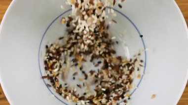 Salata tohumu karışımı beyaz bir seramik kaseye dökülür. Susam, keten, karanfil, ayçiçeği ve kabak çekirdeği. Üst Manzara. Yavaş çekim.