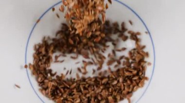 Keten tohumları beyaz bir seramik kaseye dökülür. Üst Manzara. Yavaş çekim.