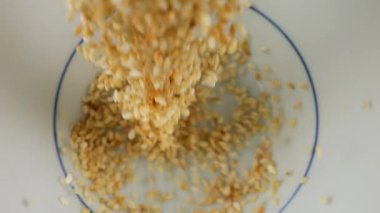 Susam tohumları beyaz bir seramik kaseye dökülür. Üst Manzara. Yavaş çekim.