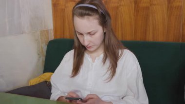 Genç bir kız restoranda bir masada oturuyor ve akıllı telefondan mesaj yazıyor..