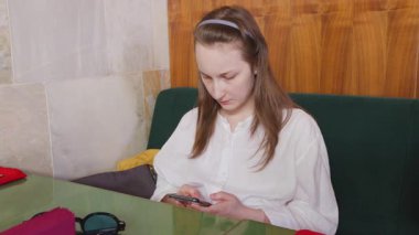 Genç bir kız restoranda bir masada oturuyor ve akıllı telefondan mesaj yazıyor..