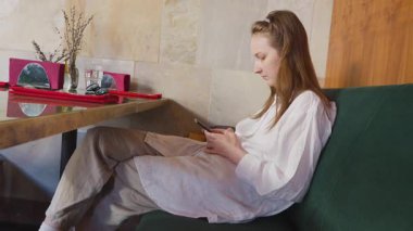 Genç bir kız restoranda bir masada oturuyor ve akıllı telefondan mesaj yazıyor..