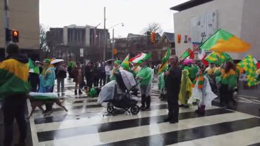 TORONTO, Kanada - 17 Mart 2025: Toronto, Ontario, Kanada 'da Aziz Patrick Günü Geçidi. Geçit törenine katılanlar, ellerinde İrlanda bayrakları, ellerinde çocuklar ve bebek arabaları, parlak kostümler, seyircilerin yanından geçiyorlar..