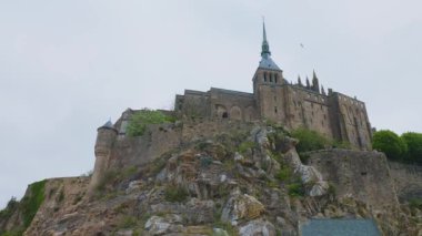 Mont-Saint-Michel Manastırı 'nın mavi gökyüzüne ve rüzgarlı bir bahar gününde bulutlara bakan manzarası. Mont-Saint-Michel Abbey, Manche ilinin Mont-Saint-Michel ilçesinde yer alan bir manastır..