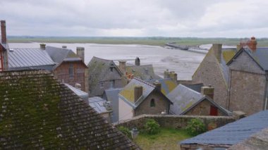 Mont-Saint-Michel Manastırı 'nın duvarlarından eski binaların kiremitli çatılarının, yeni köprünün ve rüzgarlı bir bahar gününde Manş Denizi' nin üzerine bakın..