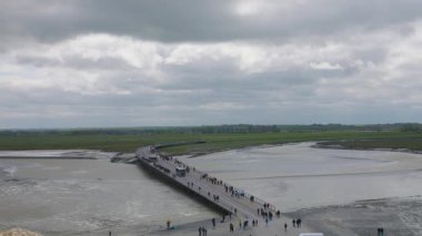 Yeni köprünün Mont-Saint-Michel Manastırı duvarlarından ve rüzgarlı bir bahar gününde turistlerin alçak gelgitte.
