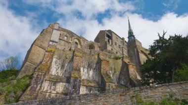 Mont-Saint-Michel Manastırı 'nın mavi gökyüzüne ve rüzgarlı bir bahar gününde bulutlara bakan manzarası.