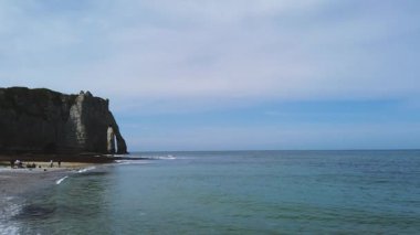Beyaz tebeşir kayalıklarının panoramik üst manzarası, deniz çekildiğinde sahilde dinlenen insanlar, doğal kemerler, bahar güneşli bir günde Etretat Tebeşir Kompleksi 'ndeki Pisseuses de Valaine plajı, Manche Kanalı (İngiliz Kanalı), Normandiya, Fransa.