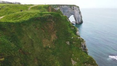 Panoramik beyaz tebeşir kayalıkları manzarası, yeşil yamaçlar, doğal kemerler ve Le Manneporte kayalıkları arasında yürüyen turistler bahar güneşli bir günde Etretat Tebeşir Kompleksi, la Manche Kanalı (İngiliz Kanalı), Normandiya, Fransa.