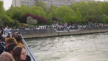 PARIS, FRANCE - 21 NİSAN 2025: Turistleri taşıyan bir yolcu gemisi, Cite Adası yakınlarındaki Seine Nehri 'nde U dönüşü yaparak parktaki sette dinlenen turistleri gözden kaçırıyor..
