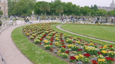 Merkezi çimlerin manzarası, Primula yatakları ve yeşil metal sandalyelerde dinlenen turistler ve Lüksemburg Baharı 'nda güneşli bir bahar gününde Fransa' nın Paris kentinde gezinen turistler..