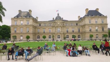 PARIS, FRANCE - 21 Nisan 2025: Turistler yeşil metal koltuklarda dinleniyor ve Lüksemburg Sarayı 'nın arka planında Lüksemburg Sarayı ile birlikte bahar aylarında geziniyorlar..