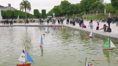 PARIS, FRANCE - 21 Nisan 2025: Yetişkinler ve çocuklar Büyük Havza 'da model yelkenlileri denize indiriyorlar. Güneşli bir bahar gününde Büyük Havza ve Lüksemburg Bahçeleri 'nin panoramik manzarası. 6. Bölge, Paris.