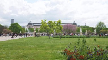 PARIS, FRANCE - 21 Nisan 2025: Baharda Tuileries Garden 'da güzel heykeller, çiçek açan ağaçlar, çiçek tarlaları ve Louvre manzarası.