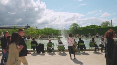 PARIS, FRANCE - 20 Nisan 2025: İnsanlar yeşil metal sandalyeli büyük bir havuz etrafında oturur ve güneşli bir bahar gününde parkın, Louvre 'un ve Eyfel Kulesinin manzarasının tadını çıkarırlar..