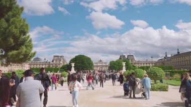 PARİS, FRANCE - 21 Nisan 2025: Turist kalabalığı baharda Tuileries Park 'ta geziniyor ve açık bir günde arka planda Louvre ile fotoğraf çekiyor.