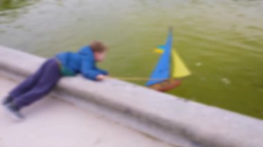 Küçük bir çocuk sarı ve mavi yelkenli bir yelkenliyi itiyor ve direğe bir çubukla Ukrayna bayrağı asıp Büyük Havza 'da yelken açıyor. Lüksemburg Bahçeleri, 6. Bölge, Paris. Odaklanamıyorum. Paris, Fransa.