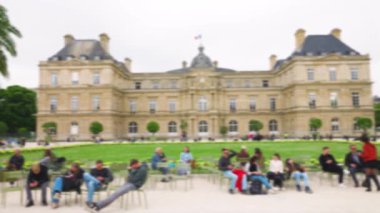 Paris 'in başkenti Paris' te güneşli bir bahar gününde, arka planda Lüksemburg Sarayı ile yeşil metal koltuklarda dinlenen ve Lüksemburg Bahçesinde gezinen turistler. Odaklanamıyorum. Paris, Fransa.