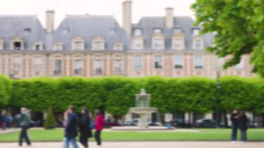 Place des Vosges 'da yürüyen insanlar. Güzel Place des Vosges 'deki dört Cortot çeşmesinden birine bakın. Ağaçlar ve arka planda eski tarihi binalar var. Paris, Fransa. Odaklanamıyorum.
