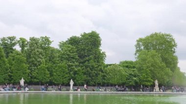 Paris, Fransa 'nın başkenti Paris' te bulutlu bir ilkbahar gününde insanlar Jardin des Tuileries 'teki çeşmeyle Grand Bassin Rond' da yürüyüp rahatlıyorlar. Çiçek açan kestane ağaçlarına ve bahçenin merkez sokağına bakıyorum..