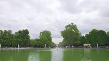 Paris, Fransa 'nın başkenti Paris' te bulutlu bir ilkbahar gününde insanlar Jardin des Tuileries 'teki çeşmeyle Grand Bassin Rond' da yürüyüp rahatlıyorlar. Çiçek açan kestane ağaçlarına ve bahçenin merkez sokağına bakıyorum..