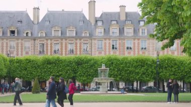 PARIS, FRANCE - 21 Nisan 2025 Vosges Meydanı 'nda yürüyen insanlar. Ağaçlı Vosges Meydanı 'ndaki dört Cortot çeşmesinden birine ve arka planda eski tarihi binalara bakın..