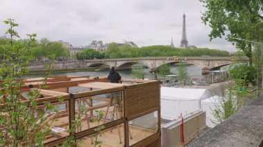 PARIS, FRANCE - 21 Nisan 2025 İşçiler Seine nehrinin sağ kıyısındaki toprak setine yeni pavyonun ahşap yapılarını dikiyorlar. Pont des Invalides ve Eyfel Kulesi 'nin manzarası.