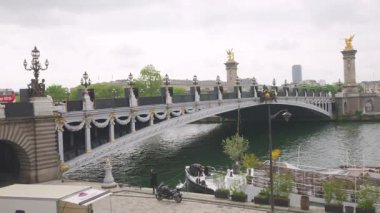 PARIS, FRANCE - 21 Nisan 2025: Seine Nehri üzerindeki Pont Alexandre III köprüsü, set ve nehrin sağ kıyısında demirlemiş bir tekne manzarası.