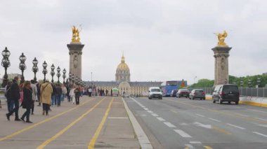 PARIS, FRANCE - 21 Nisan 2025: İnsanlar ve arabalar Hotel des Invalides manzaralı Pont Alexandre III köprüsünden Seine Nehri 'ni geçtiler.