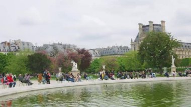 PARIS, FRANCE - 21 Nisan 2025: Birinci bölgede bulutlu bir ilkbahar gününde, Jardin des Tuileries Bahçesi 'ndeki Büyük Basin Rond (Büyük yuvarlak havuz) etrafında yürüyen ve rahatlayan insanlar.
