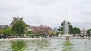PARIS, FRANCE - 21 Nisan 2025: İnsanlar Jardin des Tuileries 'deki Grand Bassin Rond' da 1. bölgede bulutlu bir bahar gününde çiçek açan ağaçlara ve Zafer Takı 'na dikkatle bakarak yürüyüp rahatlıyorlar..