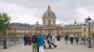 PARIS, FRANCE - 21 Nisan 2025: İnsanlar bulutlu bir bahar gününde Fransa Enstitüsü manzarası ile Pont des Arts köprüsündeki banklarda yürüyüp dinleniyorlar.