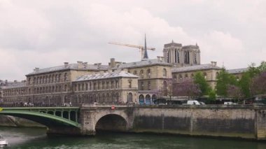 PARIS, FRANCE - 21 Nisan 2025: Seine nehri manzarası, Pont Notre Dame köprüsü, katedral kilisesi Notre-Dame de Paris ve bulutlu bir bahar gününde bir yolcu gemisi.