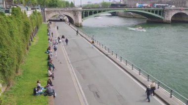 PARIS, FRANCE - 21 Nisan 2025: Seine nehri üzerindeki Pont Notre Dame köprüsünün manzarası, bulutlu bahar gününde Voie Georges Pompidou sokağında yürüyen tekne ve insanlar.