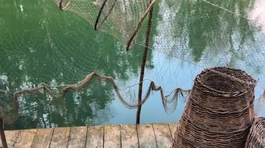 Üzerinde balık sepetleri olan ahşap bir iskele ve gölün arka planında asılı antika balıkçı ağları..