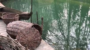 Antik ahşap balıkçı teknesi ve hasır balık sepetleri göl kıyısında.