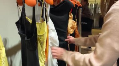 Beğendiği şeyleri seçmek için kayışlı yaz kokteyl elbiselerinin modellerine bakan bir kız. Lüks Fransız mağazası Galeri Lafayette Haussmann, Paris, Fransa.